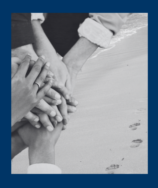 hands stacked together over sandy beach